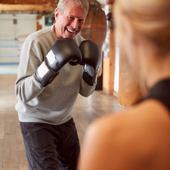 Senior Male Boxer Sparring With Younger Female Coach In Gym Using Training Gloves